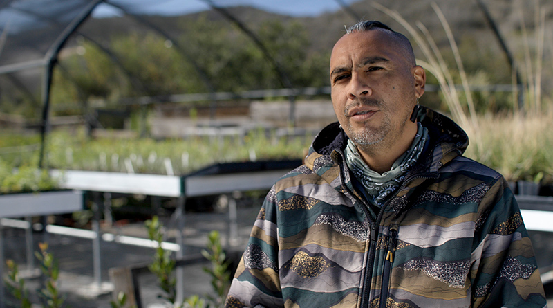 Man sitting in front of a greenhouse