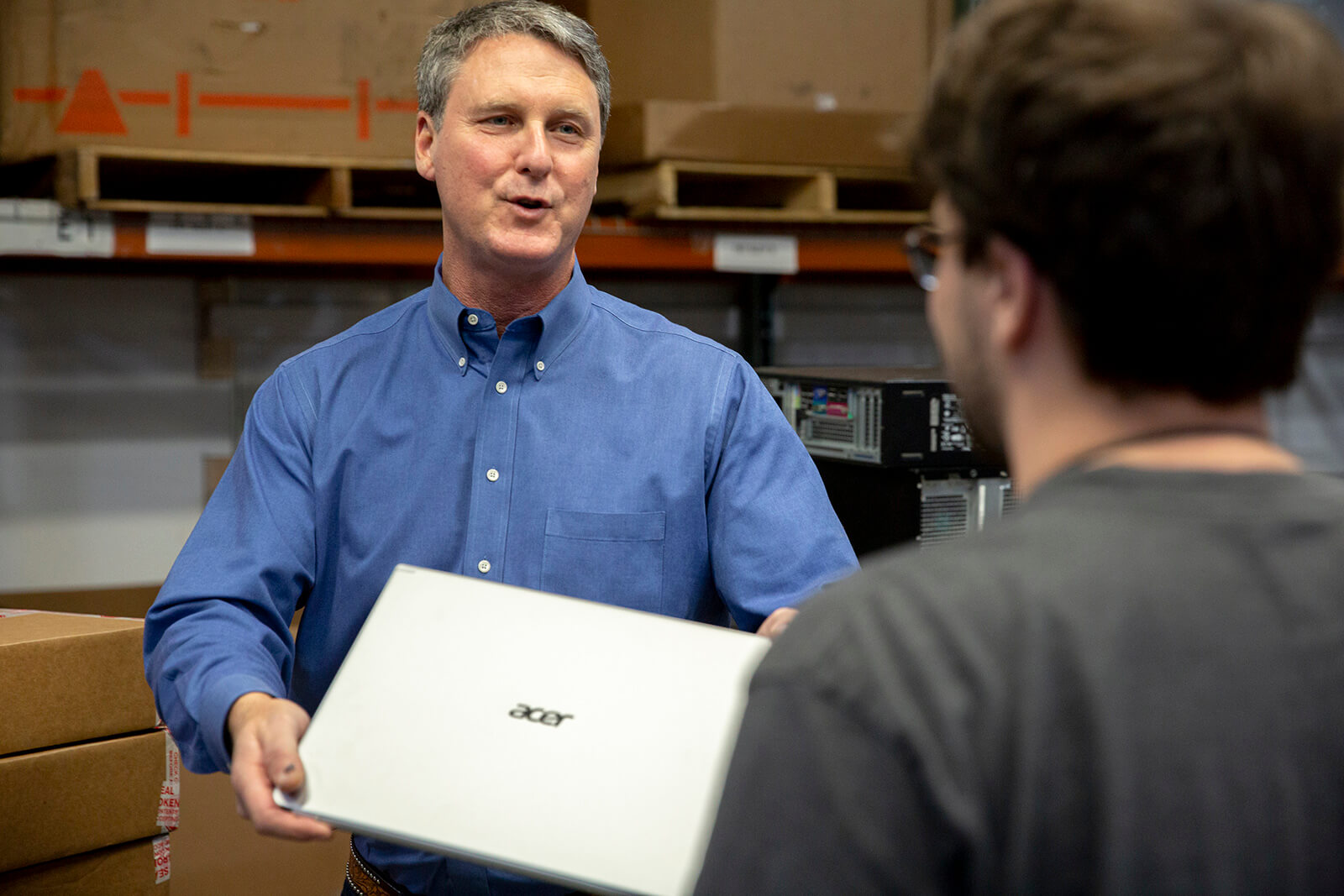 Man handing a laptop to another person